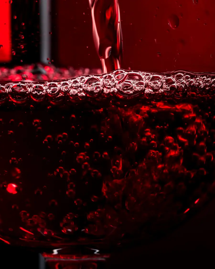 Red wine being poured into a glass, close up, with bubbles rising at the surface